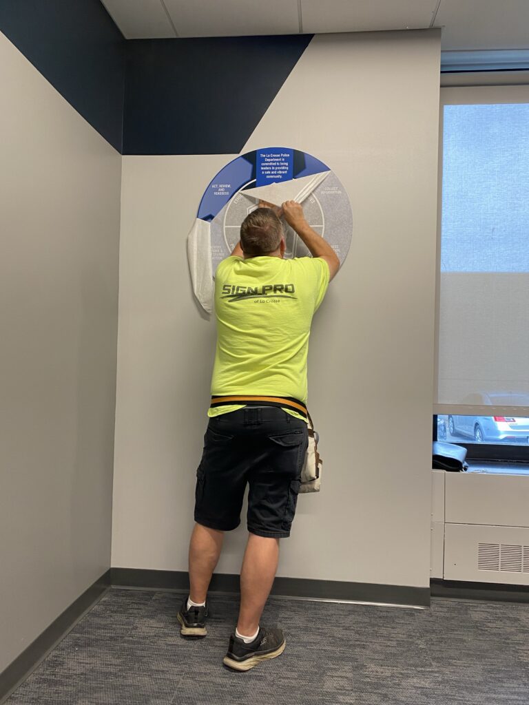 Sign Pro team member installing custom interior signage for the La Crosse Police Department. 