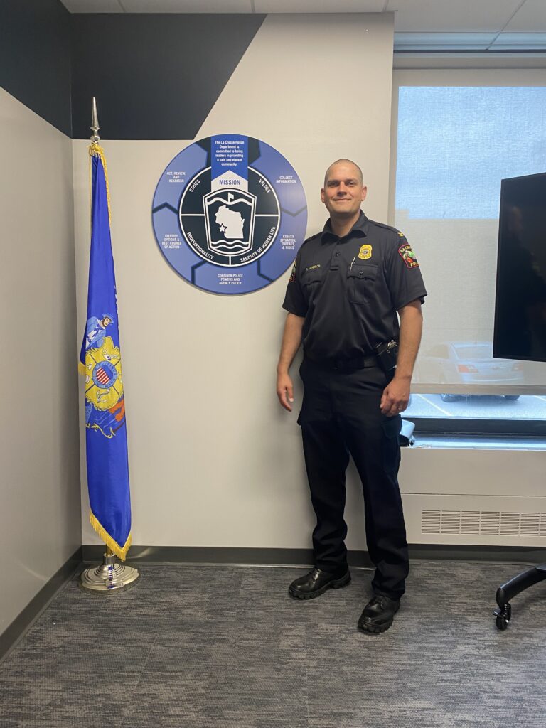 La Crosse Chief of Police Shawn Kudron, standing in front of new custom interior signage of CDM (critical decision-making model) which was designed, manufactured, and installed by Sign Pro of La Crosse, WI.