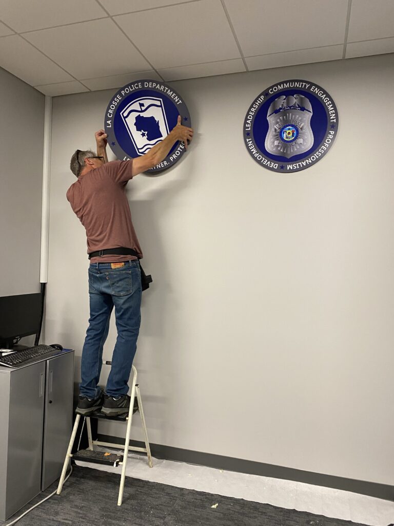 Sign Pro team member installing custom interior signage for the La Crosse Police Department. 