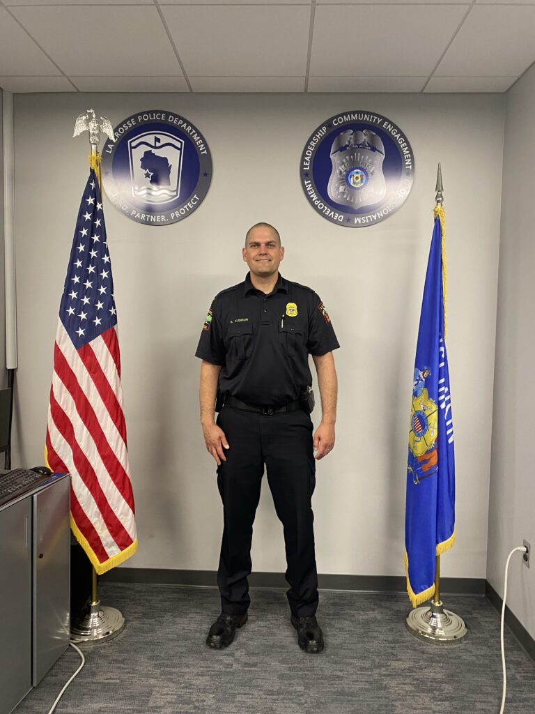 La Crosse Chief of Police Shawn Kudron standing in front of new custom interior signage that was designed, made, and installed all by Sign Pro of La Crosse, WI.